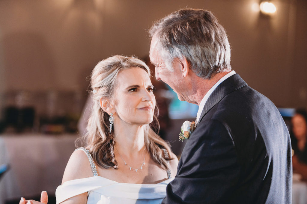 blonde bride smiles at silver haired groom during their first dance during their five willows wedding