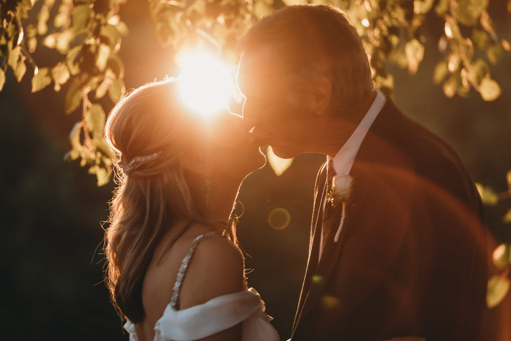 bride and groom kiss at sunset with sunlight shining between them during their five willows wedding