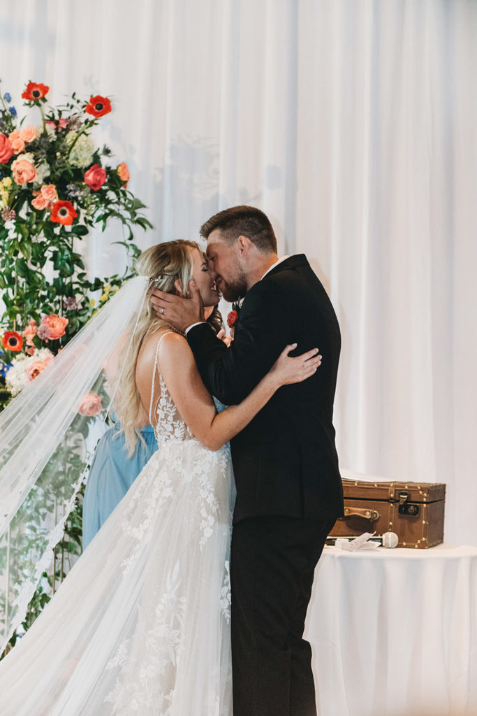 bride and groom kiss in front of flowers during their charming mavris wedding