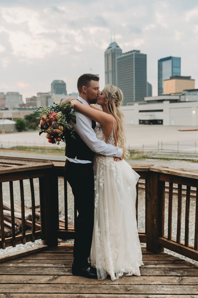 bride and groom kiss in front of indy skyline during their charming mavris wedding