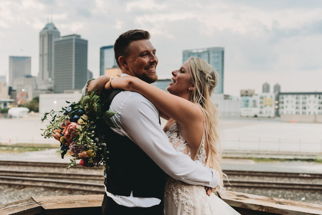 bride and groom hug and laugh in front of indy skyline during their charming mavris wedding