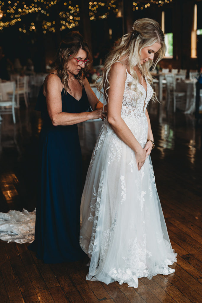 bride is helped into wedding dress by mother during her charming mavris wedding