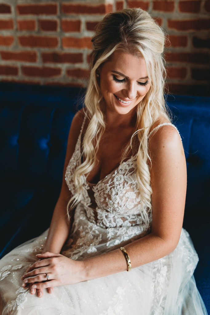blonde bride in white dress smiles in front of brick wall during her charming mavris wedding