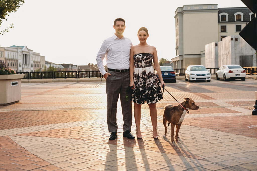 a man and a woman and their dog backlit by sunset during their Carmel City Center engagement session