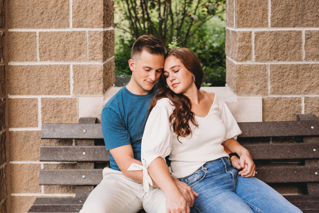 man and woman snuggle on bench during their eagle creek park engagement session