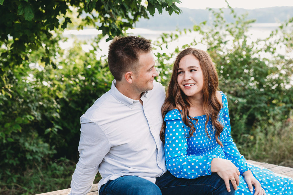 man with short brown hair sits on picnic table with woman with long brown hair during their eagle creek park engagement session