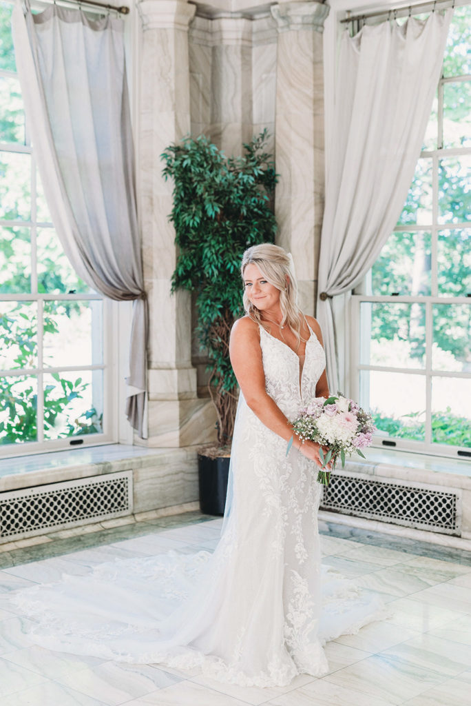 bride looks over shoulder while holding flowers inside gorgeous white marble building during a marian university wedding