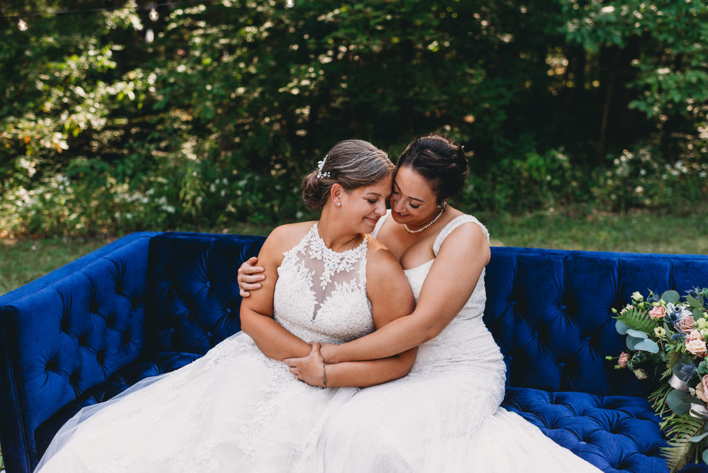 two brides hug on an antique, blue settee during their Martinsville wedding