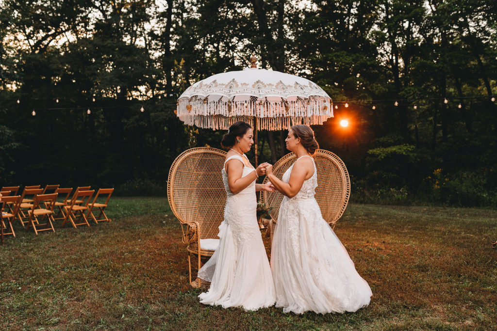 two brides dance in front of antique wicker chairs under an antique umbrella during their Martinsville wedding