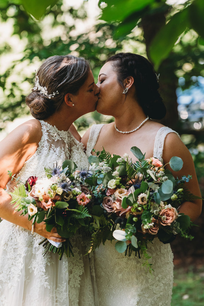 two brides with gorgeous bouquets kiss in the woods during their Martinsville wedding