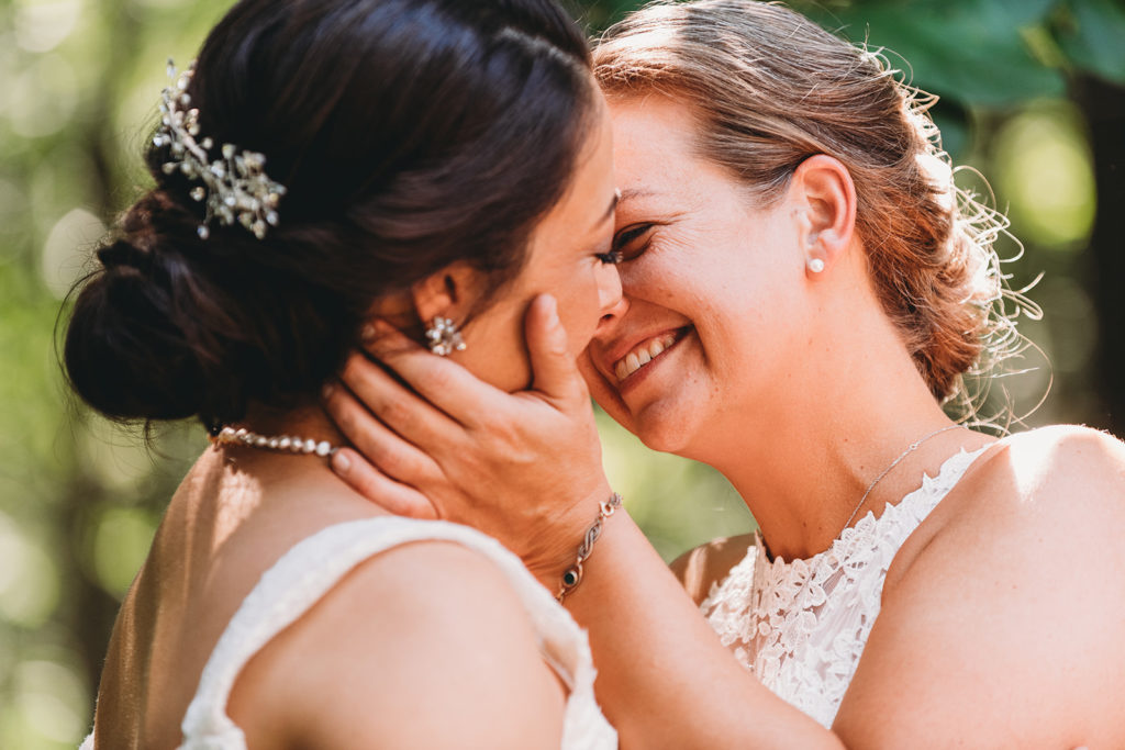 two brides kiss in the woods while one holds the other's face in her hands during their Martinsville wedding