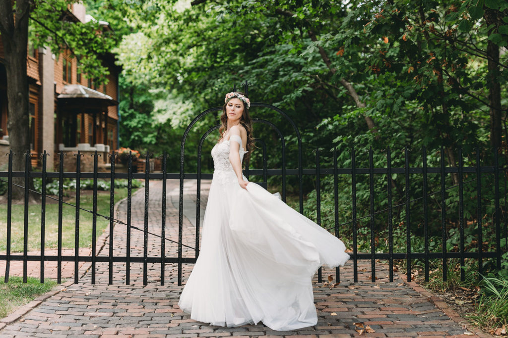 bride with gorgeous flower crown dances in front of gates while her dress catches the wind and flows around her during during Minnetrista wedding