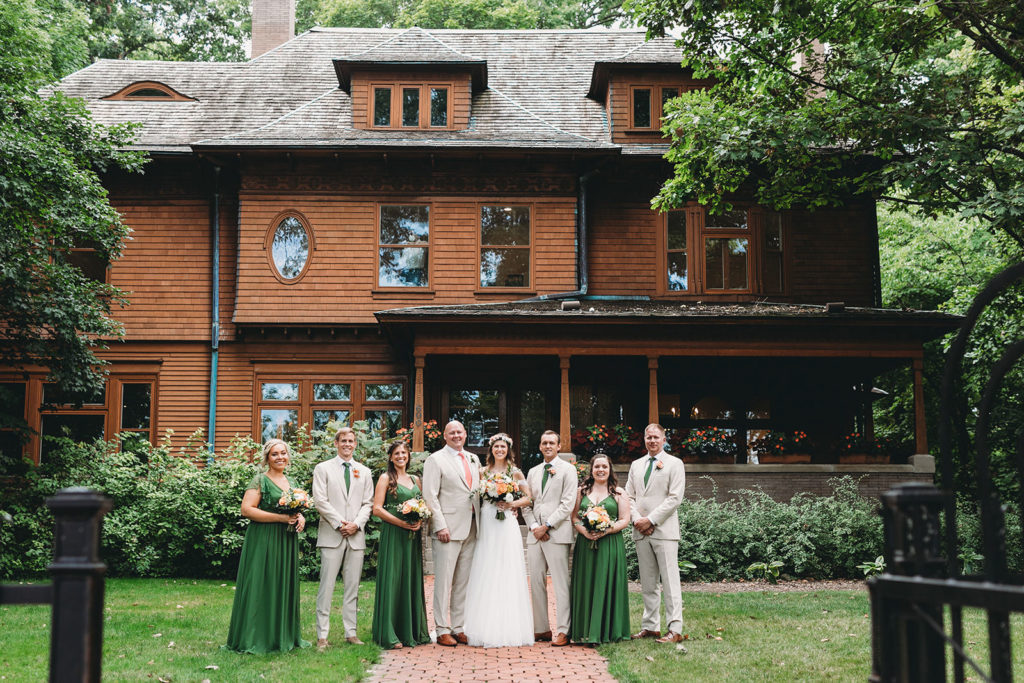 group photos in front of ball house with a masked man in the window of the house watching them during their Minnetrista wedding