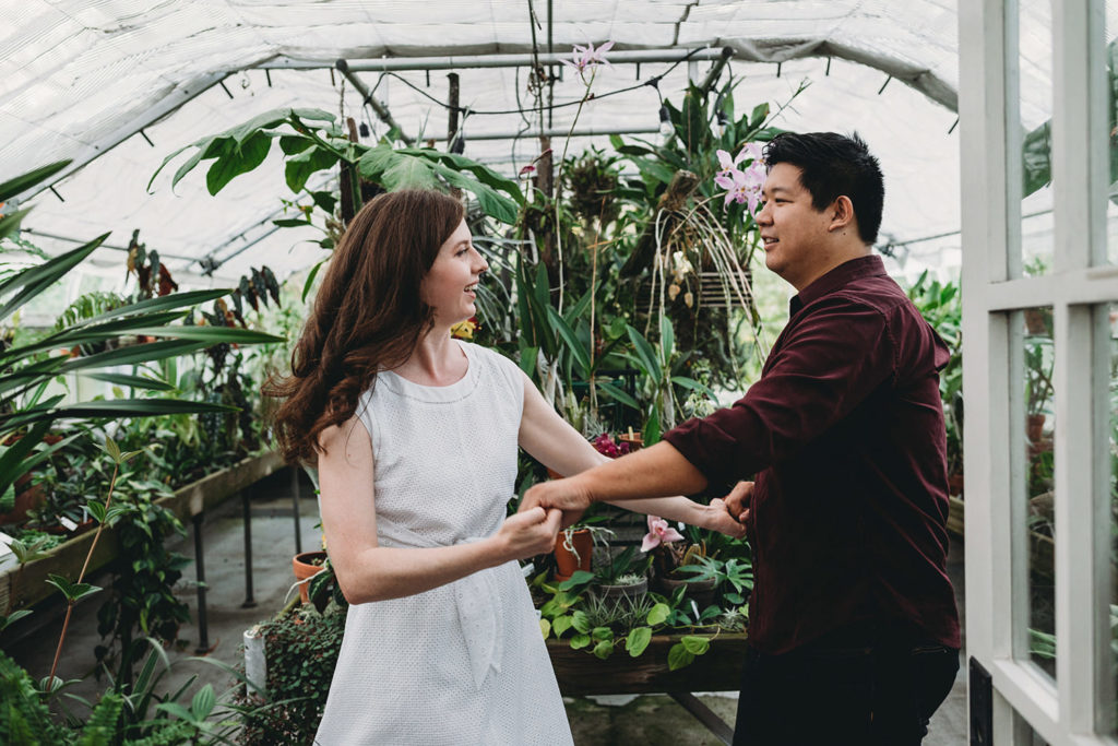 a man and a woman dance in front of a bunch of plants during their newfields greenhouse engagement photos