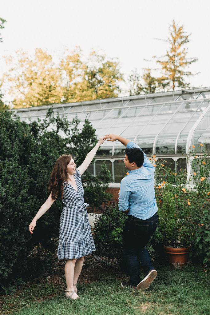 a man and a woman dance outside a glass building during their newfields greenhouse engagement photos
