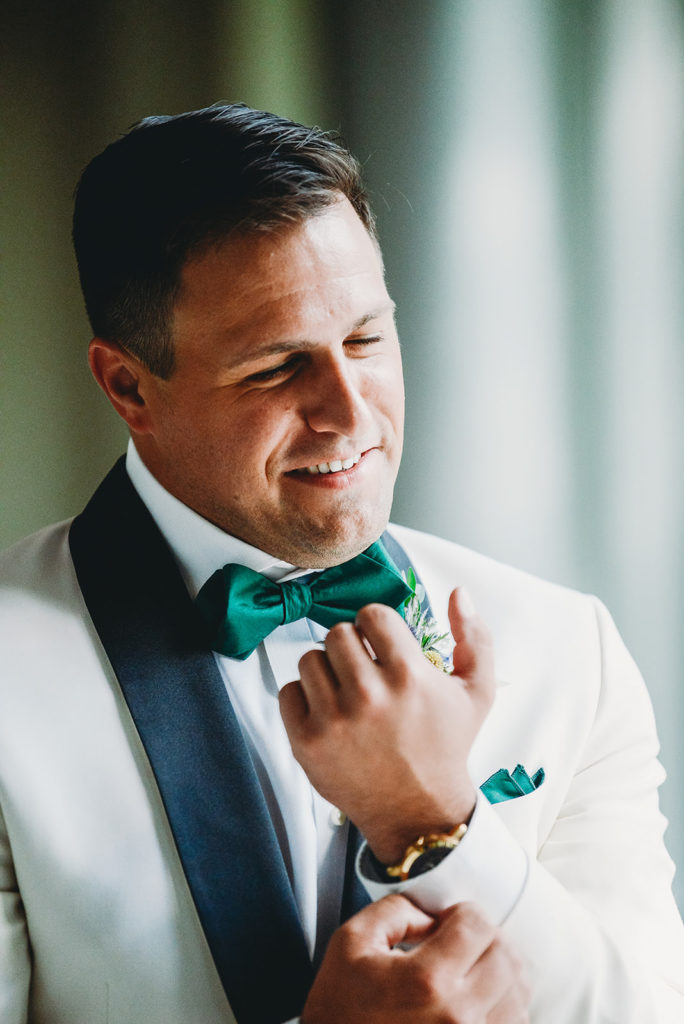 Suave groom in white tux with green bow tie before his Newfields Lilly Terrace wedding