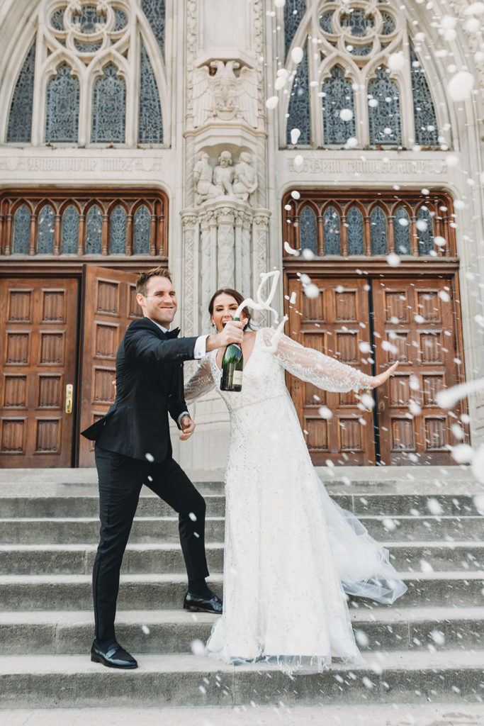 bride and groom pop open a bottle of champagne and champagne goes everywhere on the steps of the scottish rite cathedral during a scottish rite cathedral wedding