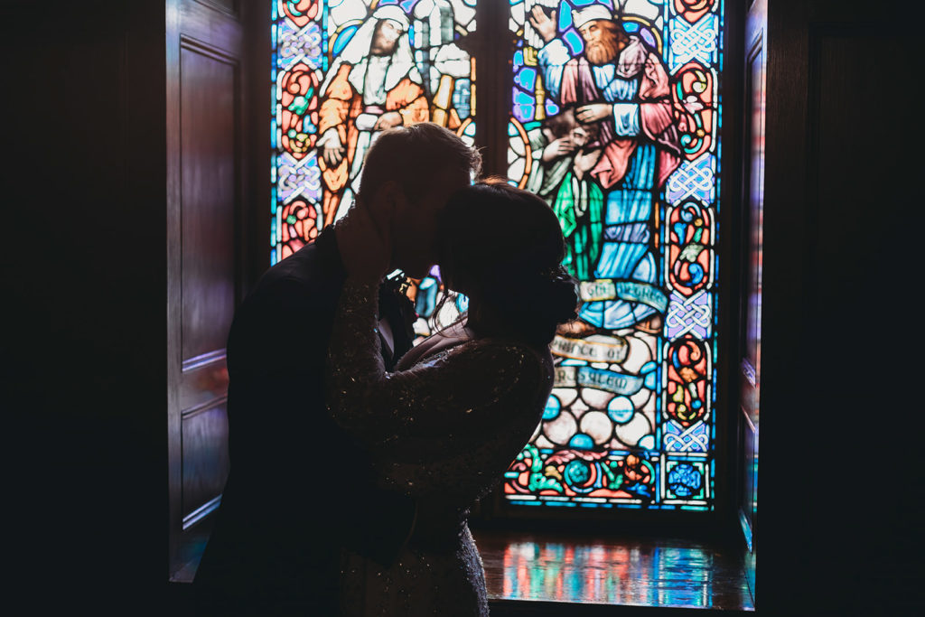 silhouette of bride and groom kissing in front of stained glass during a scottish rite cathedral wedding