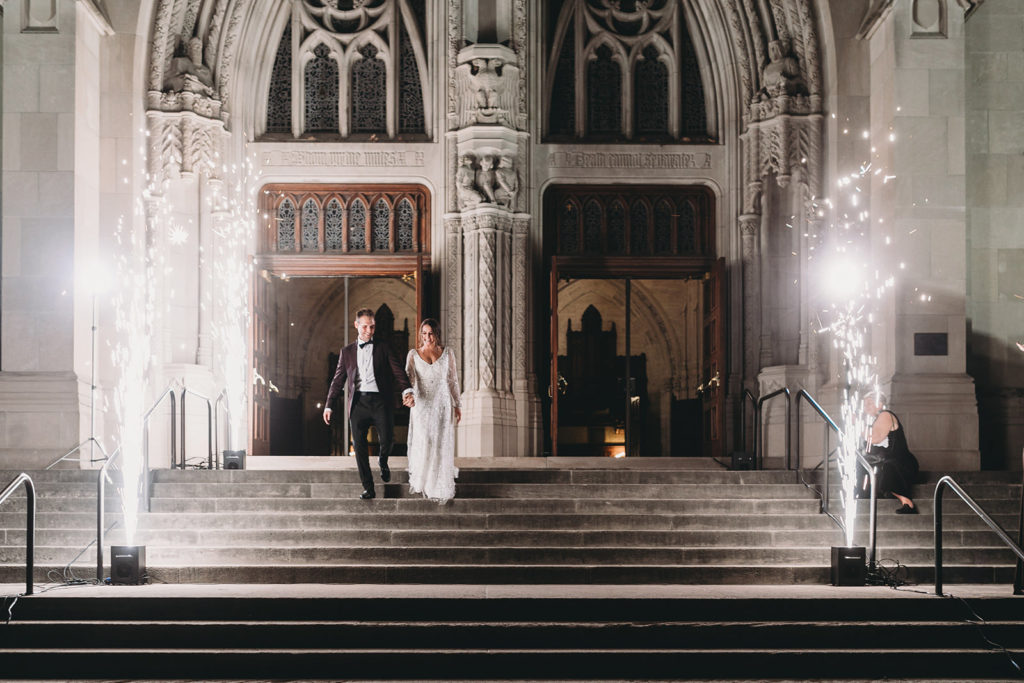 bride and groom walk down the steps of the scottish rite cathedral while ice lights shoot sparks into the air during a scottish rite cathedral wedding