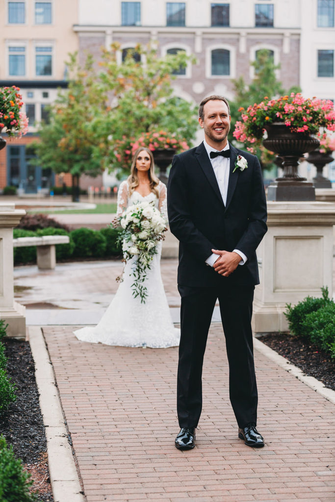 bride walks up behind groom for first look in carmel city center outside the palladium during their Artisan Acres Estate wedding