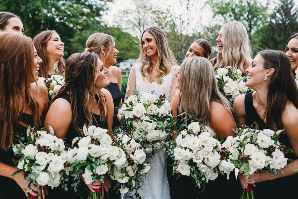 a beautiful bride holding white flowers surrounded by her bridesmaids during their Artisan Acres Estate wedding