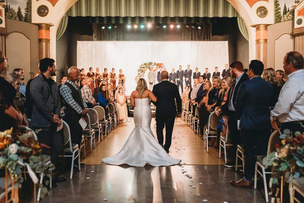 shot of bride and dad walking down the aisle from behind while their guests watch them progress through the theater during their fountain square theatre wedding