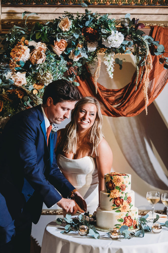 beautiful bride and handsome groom cut floral patterned wedding cake in theater during their fountain square theatre wedding