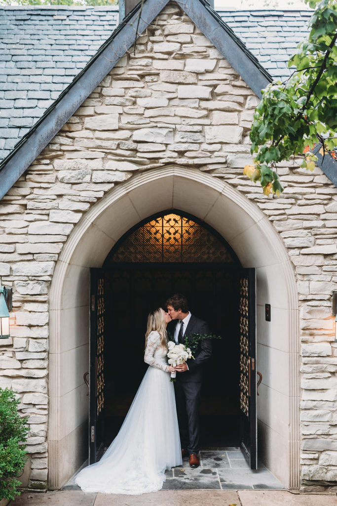bride and groom kiss in entryway to beck chapel on a rainy day during their indiana university wedding