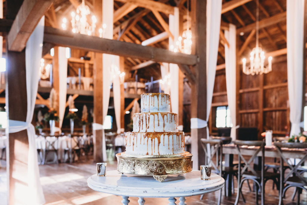 cake in front of room of tables and chairs in barn during their mustard seed wedding