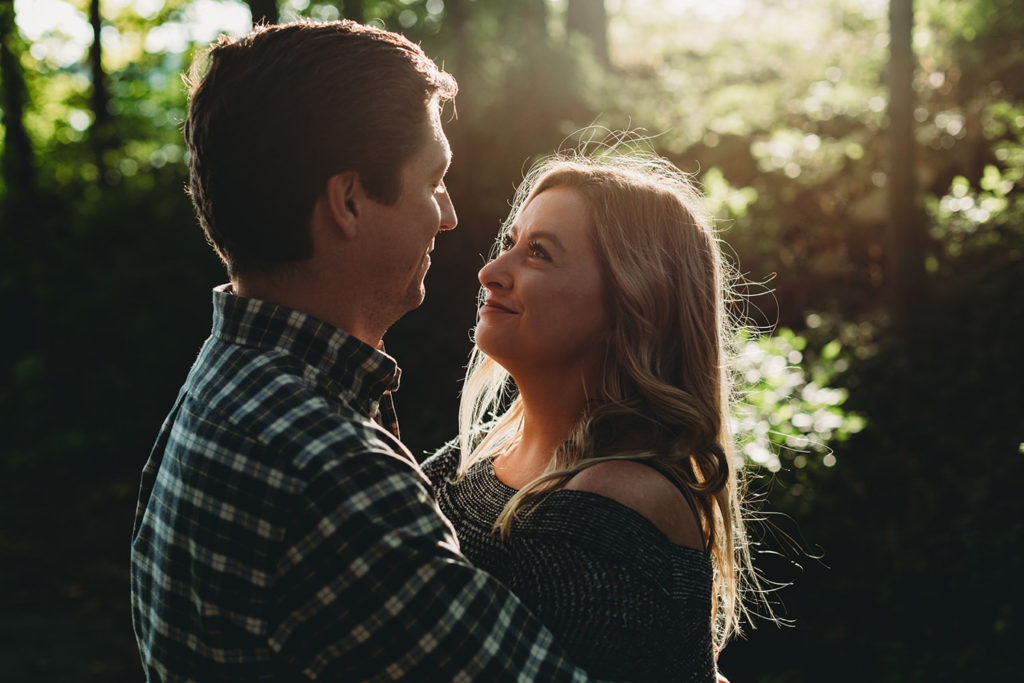 blonde woman looks at man and prepares to kiss him at sunset in the woods during their wonderful eagle creek engagement session