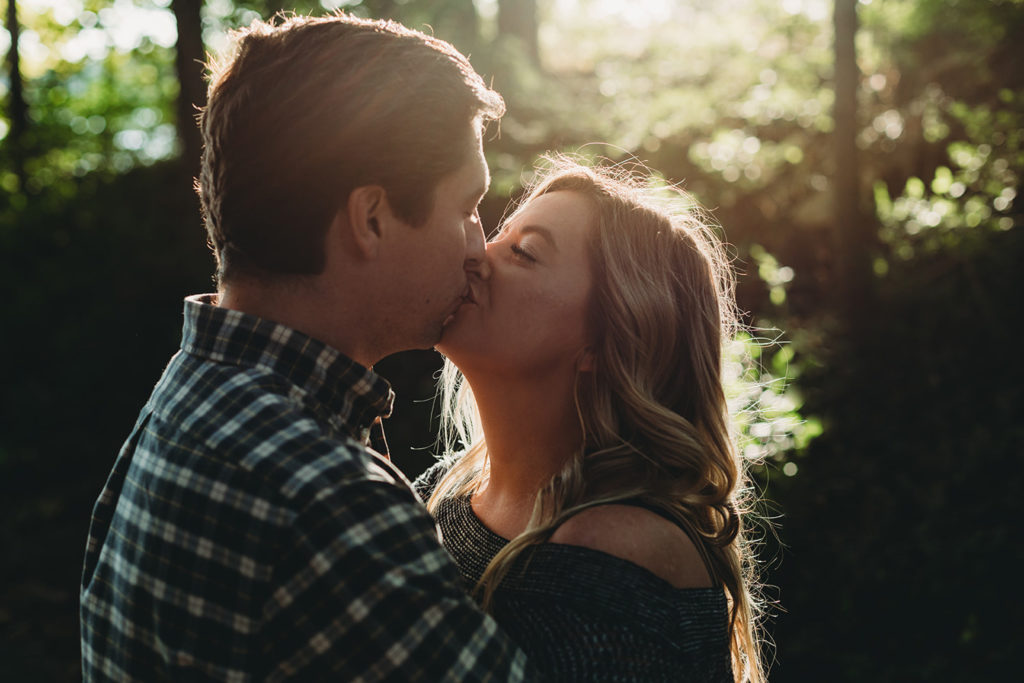 man and woman kiss in woods in a dark and moody photo during their wonderful eagle creek engagement session