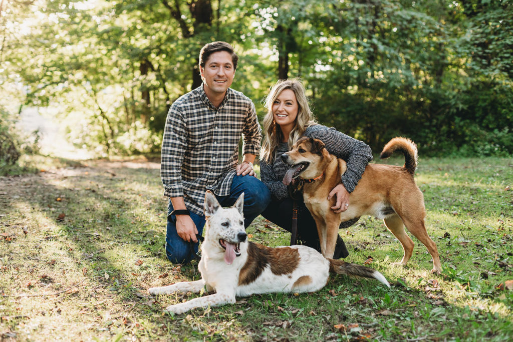 a man in a flannel shirt and a blonde woman kneel down with their dogs during their wonderful eagle creek engagement session