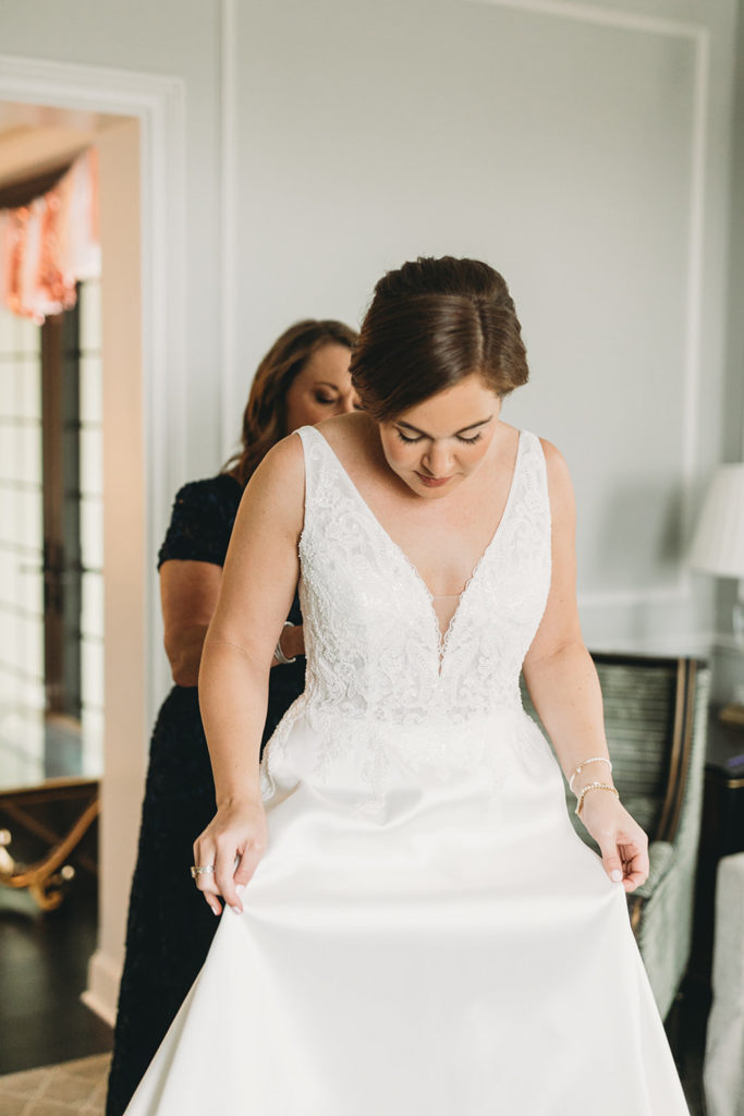 mother of bride helps bride into wedding dress during their charming carmel wedding