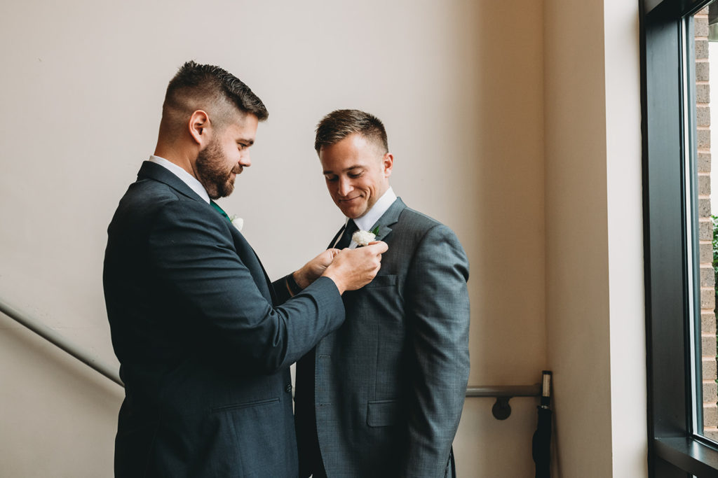 groomsman helps groom with boutonniere during their charming carmel wedding