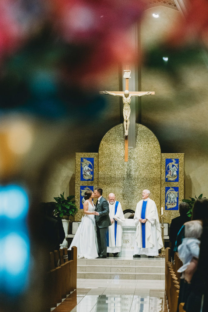 framed by flowers bride and groom share first kiss at our lady of mt carmel during their charming carmel wedding
