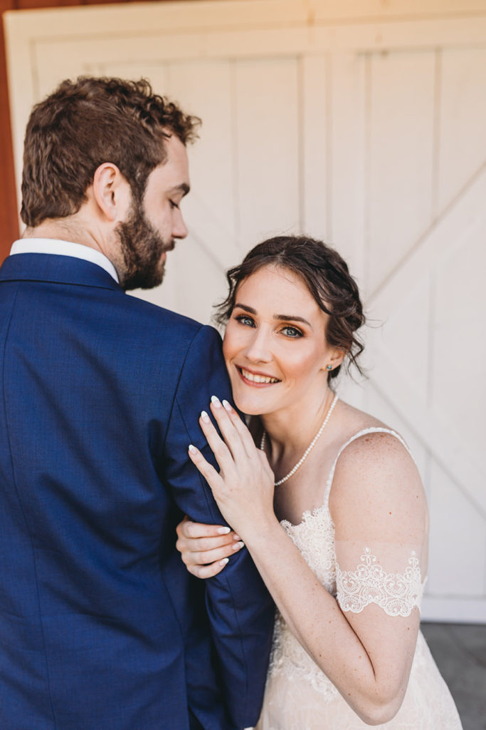 bride snuggles up to groom in front of white barn doors during their charming Lindley Farmstead wedding