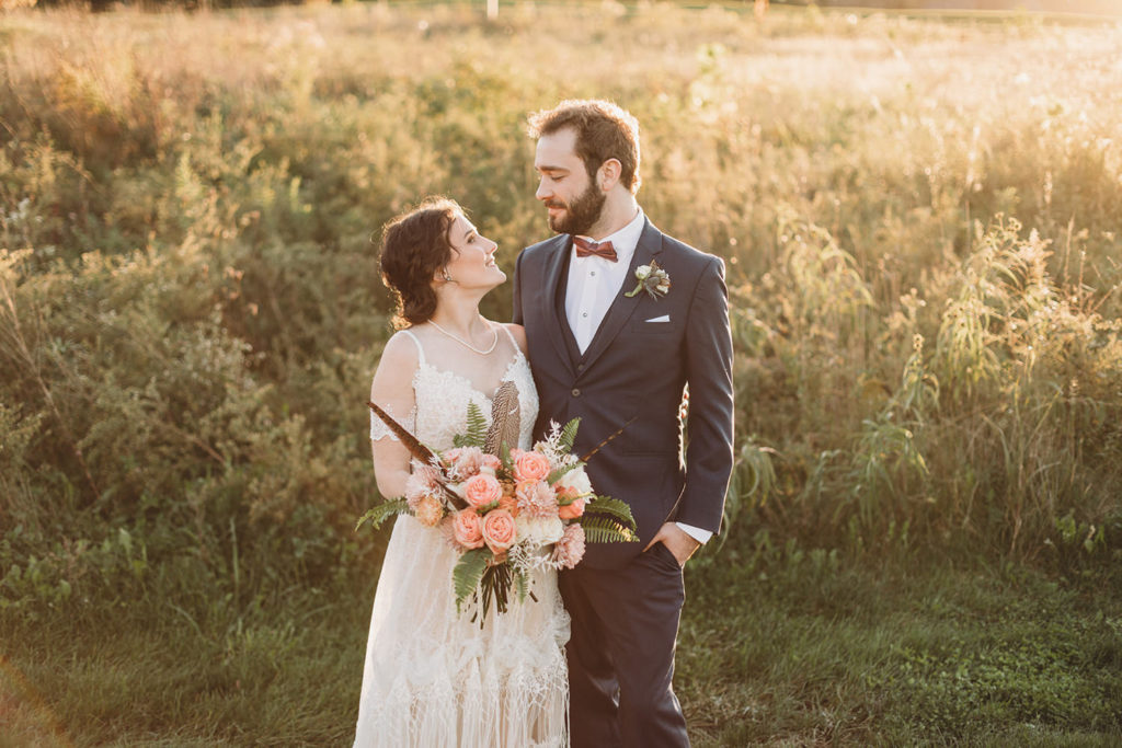bride and groom hugging and looking at each other in front of a field of wild flowers in autumn at sunset during their charming Lindley Farmstead wedding