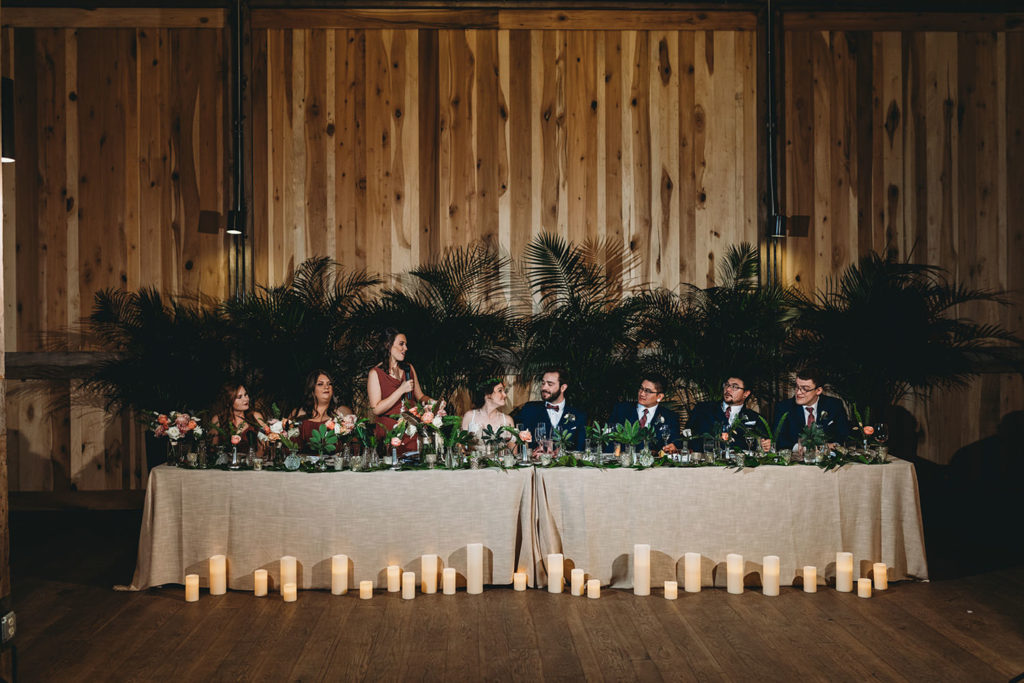 tropical plants adorn the head table and serve as a back drop behind the head table during a charming Lindley Farmstead wedding