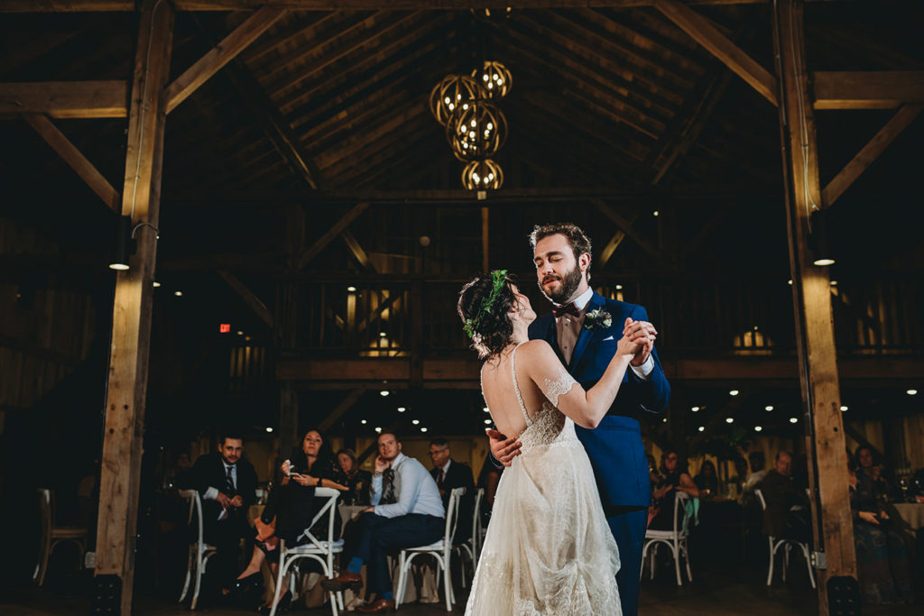 wide shot of bride and groom sharing first dance in front of guests inside an air conditioned barn during their charming Lindley Farmstead wedding