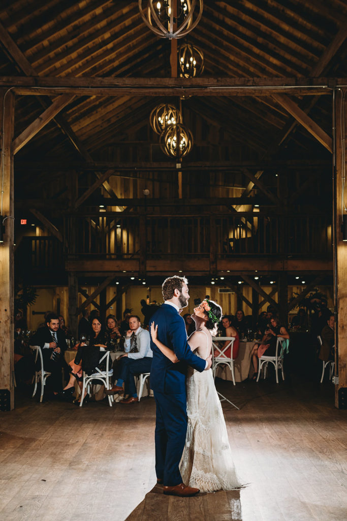 wide shot of bride and groom sharing first dance and holding each other in an air conditioned barn during their charming Lindley Farmstead wedding