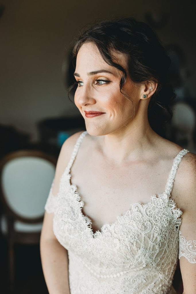 bride in window light smiling as she gets ready during their charming Lindley Farmstead wedding