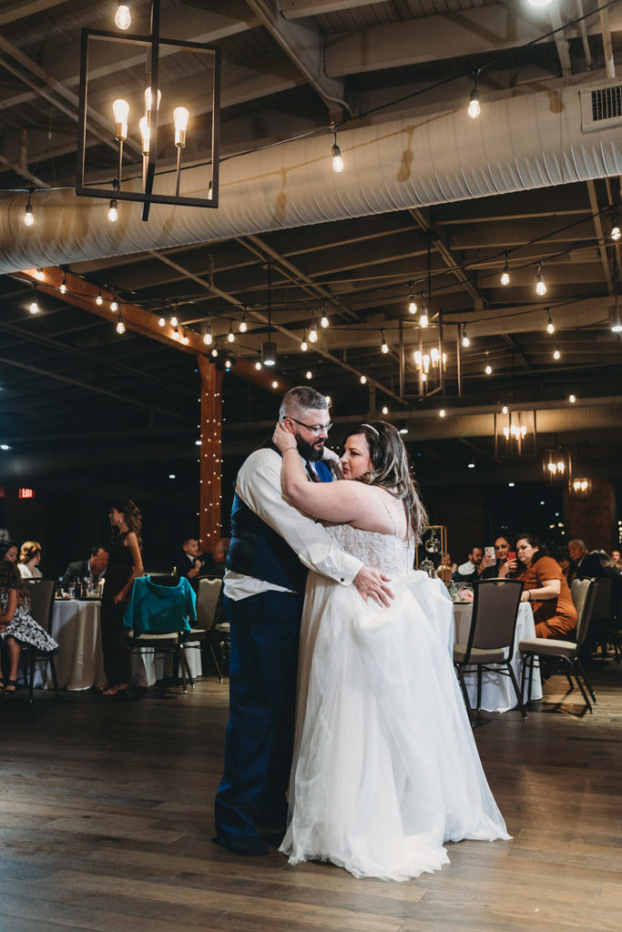 wide vertical photo of bride and groom sharing first dance during their garment factory events wedding