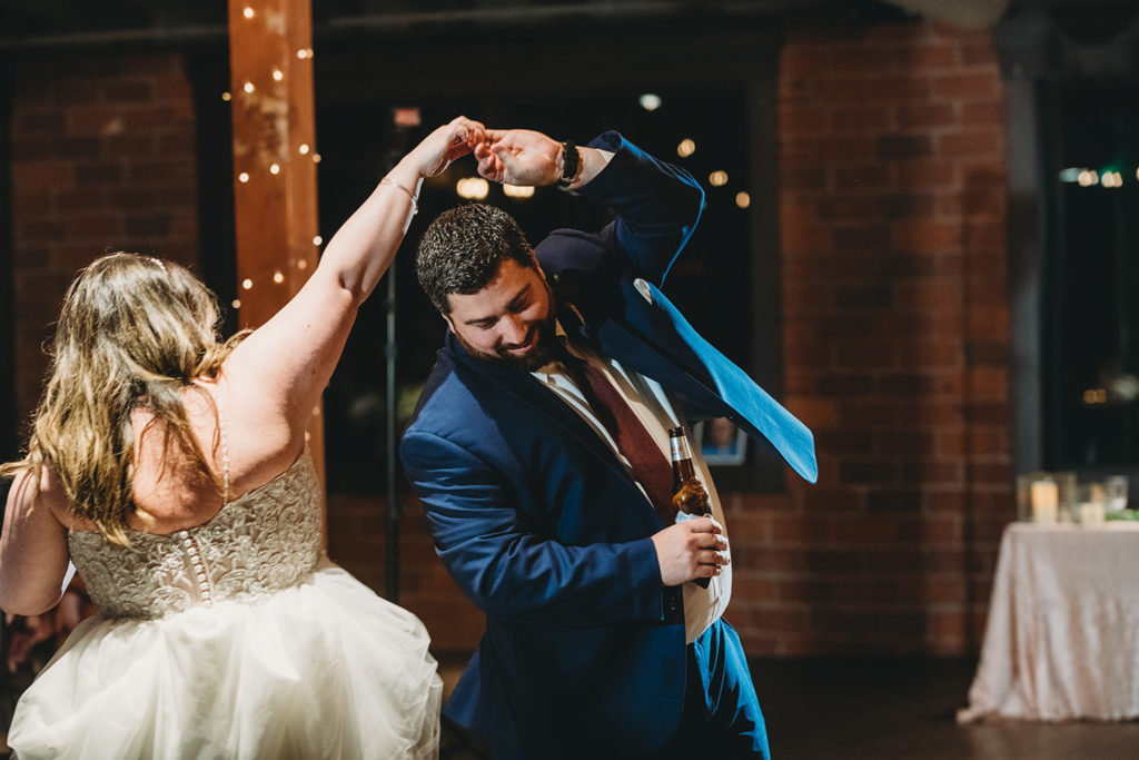 bride spins brother during the father daughter dance as they both laugh while remembering their lost father during their garment factory events wedding