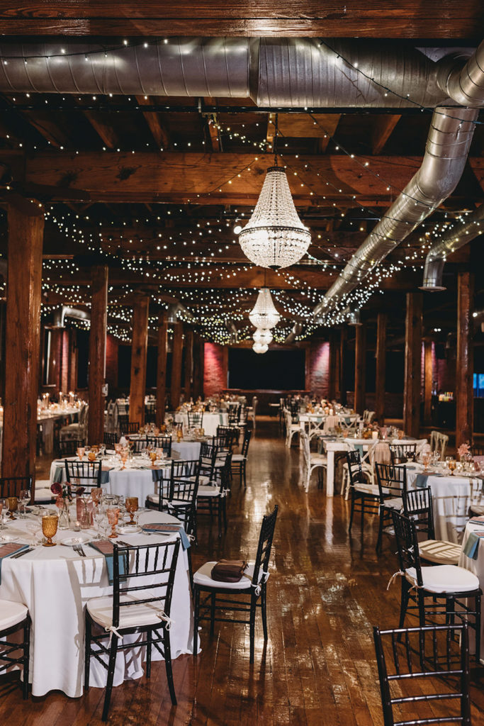 vertical photo of event space set up for wedding with square tables and circular tables intermixed during their mavris reception