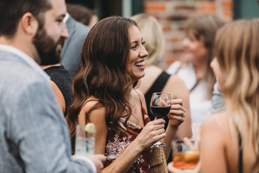 woman in red floral dress holding wine laughs during party during their mavris reception