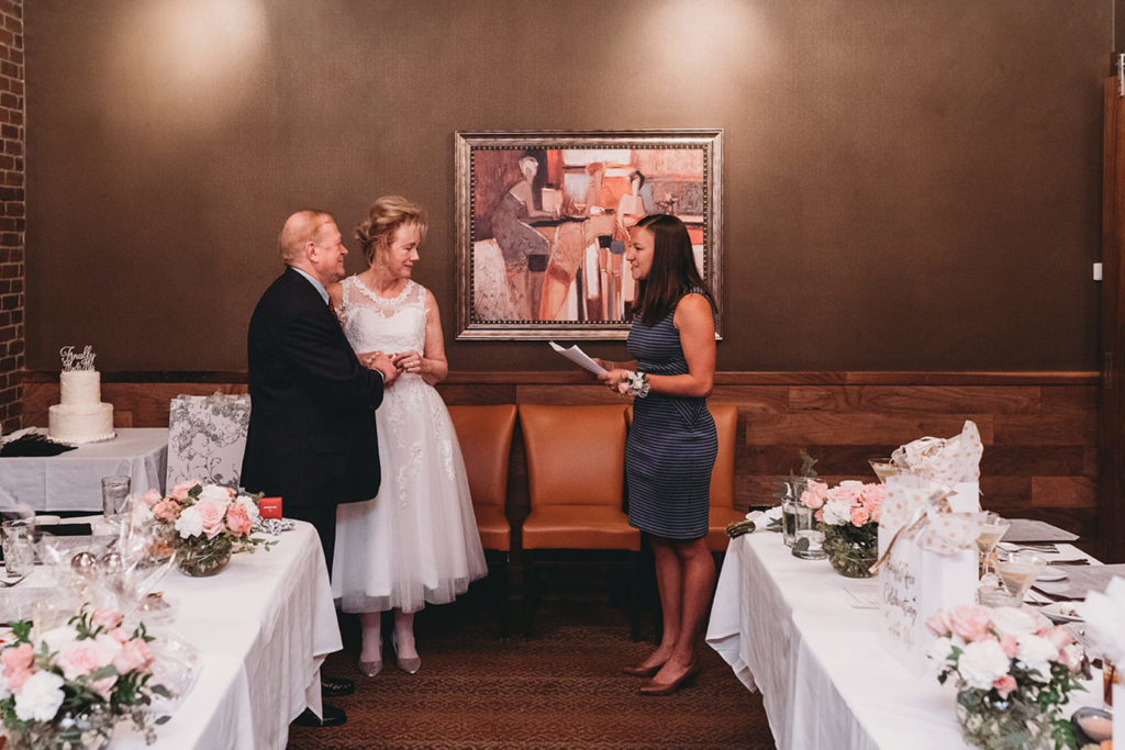 wide shot of bride and groom and officiant with art behind them during a sullivans steakhouse wedding