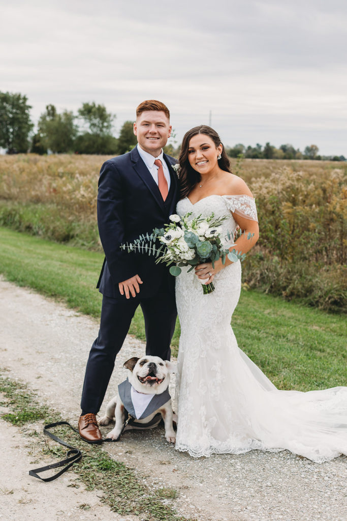 bride and groom and dog in tux in front of a field during their white willow farms wedding