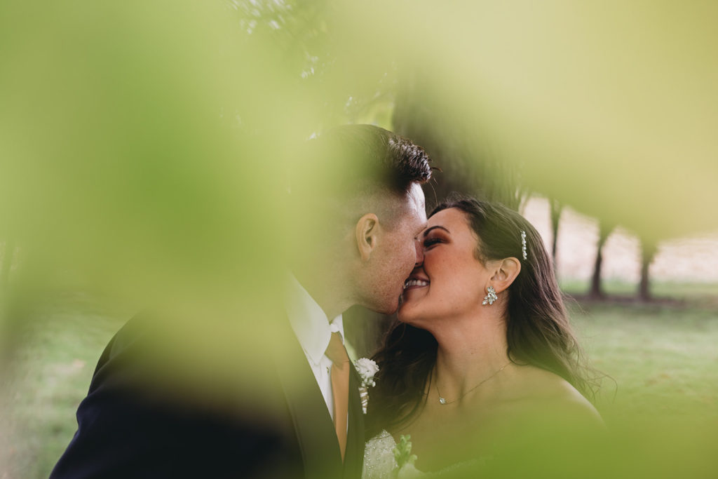 blurry leaves frame bride and groom as they kiss during their white willow farms wedding