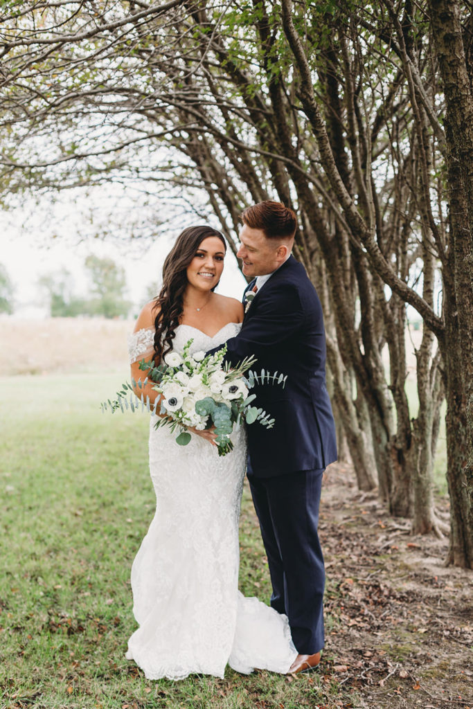 bride and groom hug next to a row of trees during their white willow farms wedding