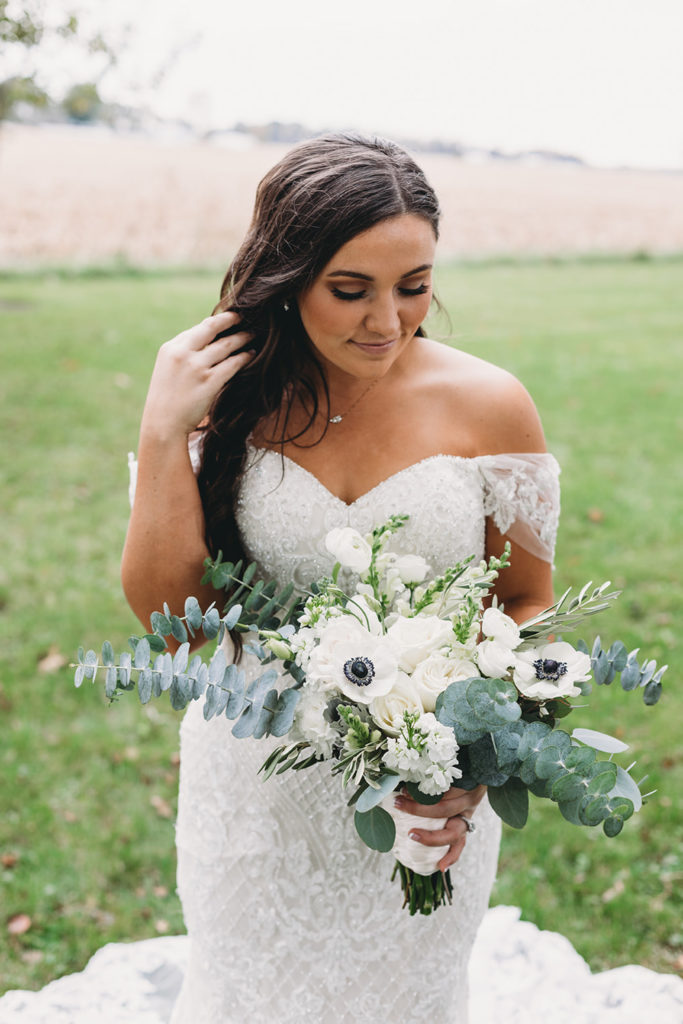 gorgeous bride holding bouquet in grass with field behind her during her white willow farms wedding